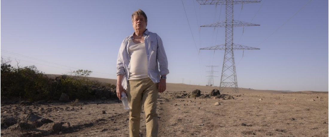 Fotograma de Amores incompletos: Alejandro Camacho de pie en un terreno árido de Baja California, bajo las torres de alta tensión