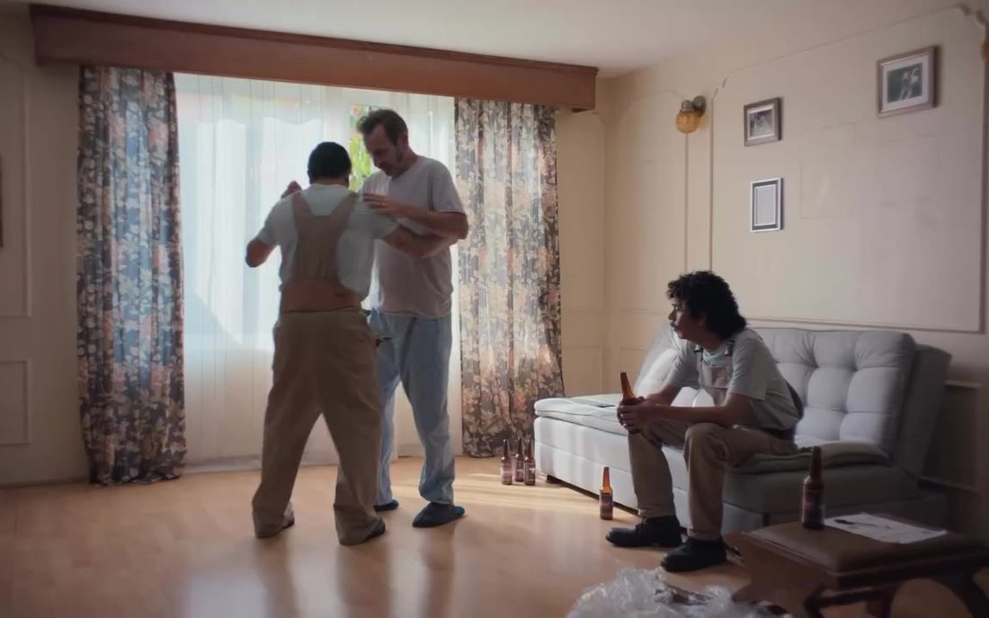 Fotograma de Bailando solo: ensayo de baile en una sala con cortinas blancas mientras un hombre observa desde el sillón