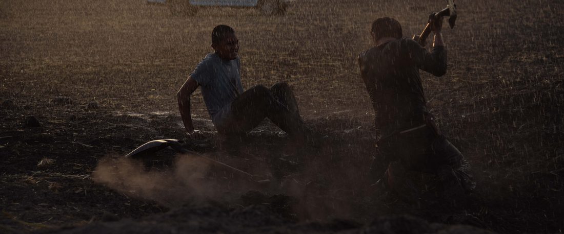 Fotograma de Vergüenza: dos jóvenes forcejean en un llano de tierra al atardecer, junto a una camioneta